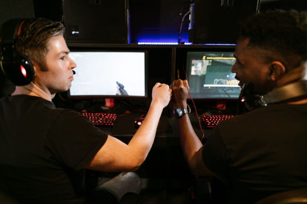 Two PC gamers with headsets bumping fists at their gaming stations